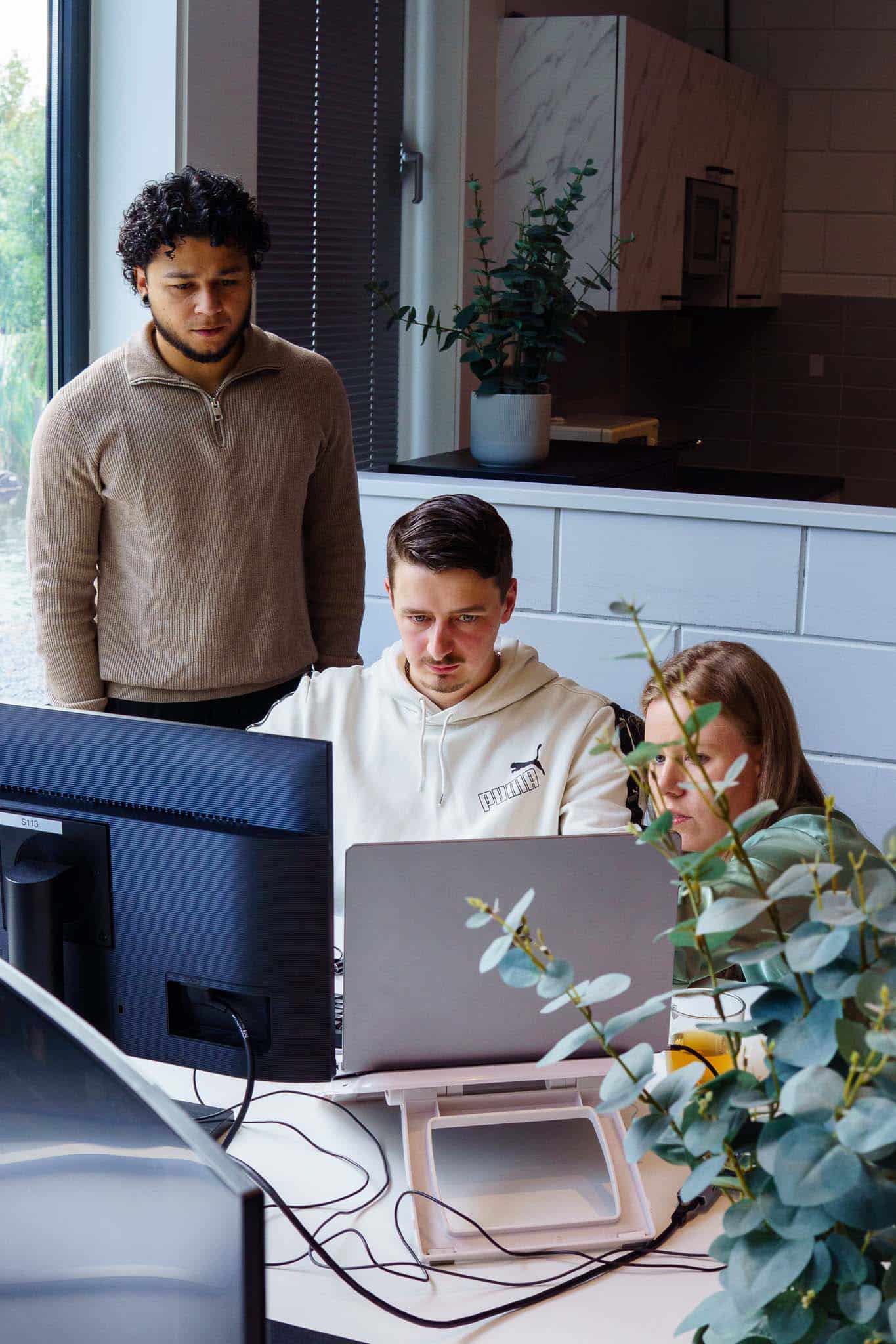 BURO210 Fullservice Marketingbureau Drie collega's werken samen aan een computer in een moderne kantooromgeving. Focus op teamwork en projectontwikkeling in een innovatieve setting.