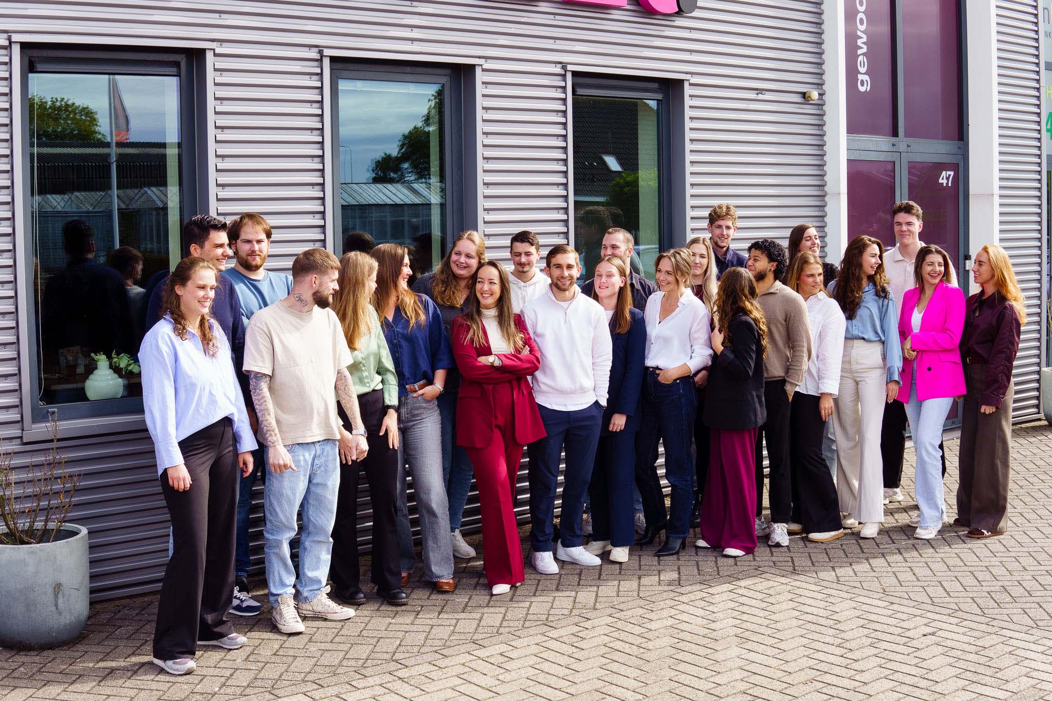 BURO210 Fullservice Marketingbureau Groepsfoto van een divers team van jonge professionals voor een modern kantoorgebouw. Bekijk de teamleden en hun betrokkenheid bij het bedrijf.