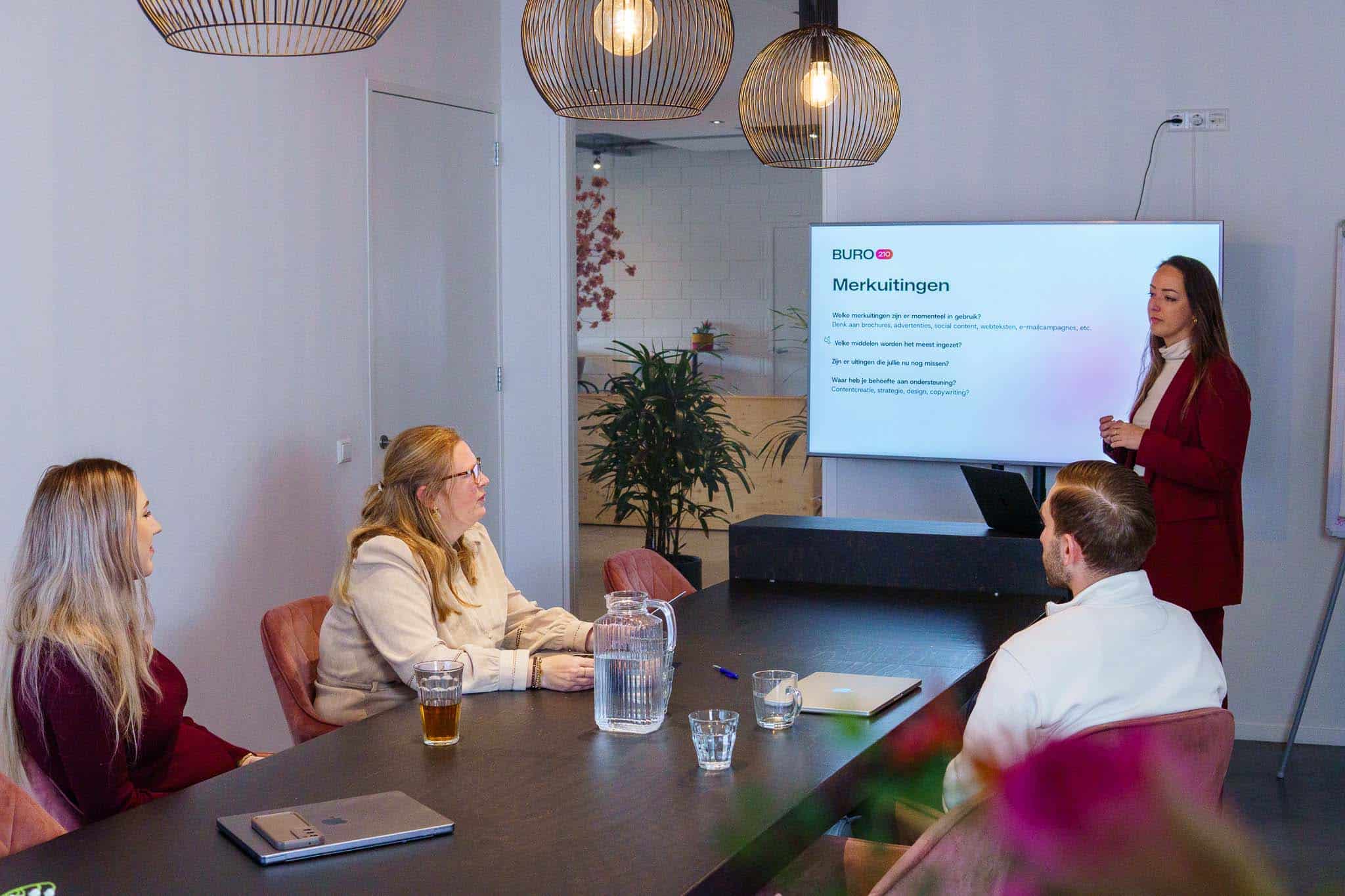BURO210 Fullservice Marketingbureau Teamvergadering bij Buro 210. Collega's bespreken merkuitingen en contentstrategieën tijdens een presentatie in een moderne vergaderruimte. Focus op branding en marketing.
