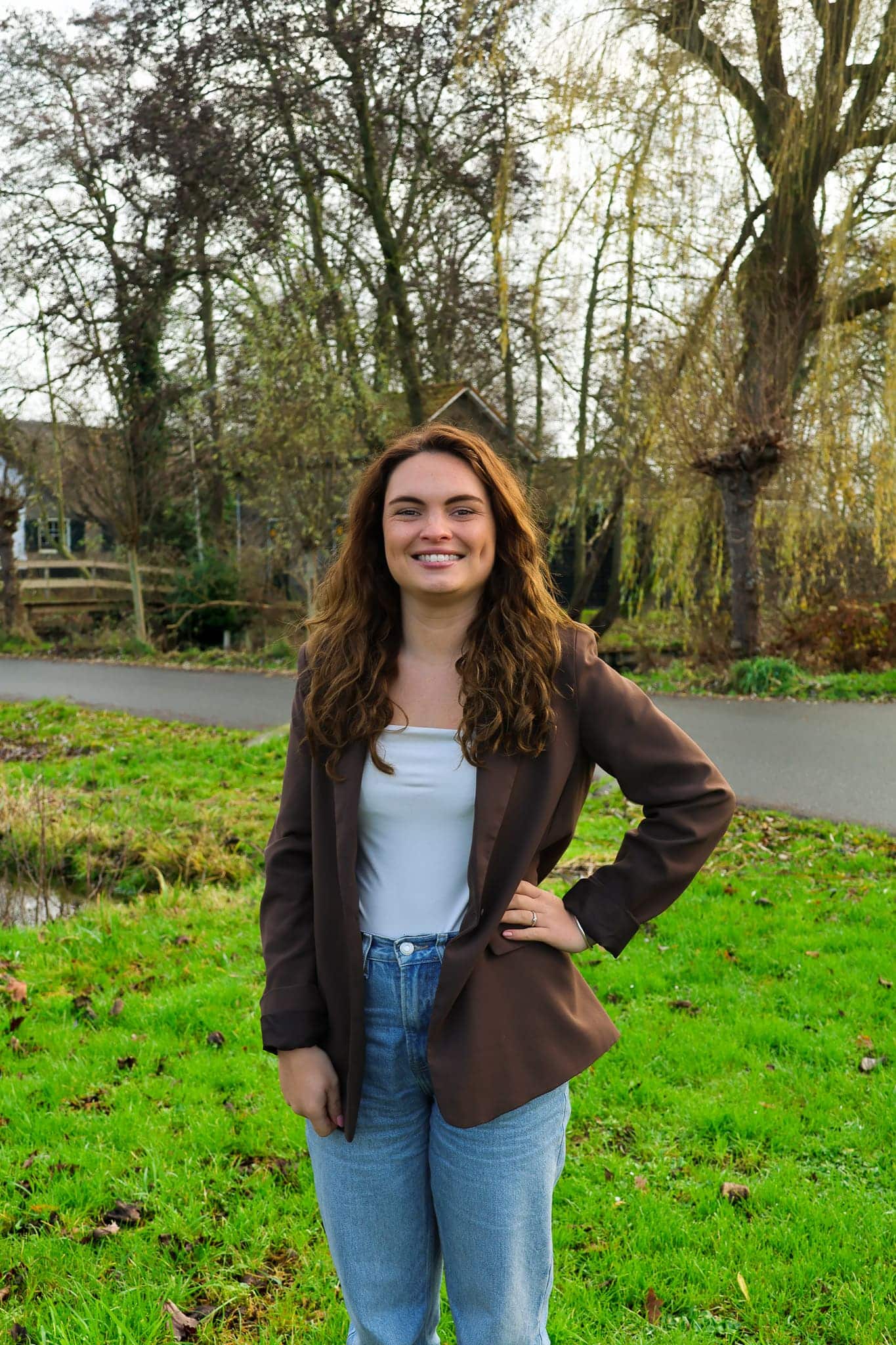 BURO210 Fullservice Marketingbureau Portret van een van onze specialisten, een vriendelijke jonge vrouw met bruin haar, gekleed in een bruine blazer, buiten in een groene omgeving.